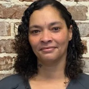 smiling woman with a grey merry maids uniform standing in front of a brick wall